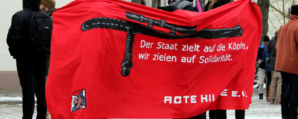 Menschen halten ein Tansparent mit der Aufschrift »Der Staat ziehlt auf die Köpfen, wir zielen auf Solidariät! Rote Hilfe e.V.«
