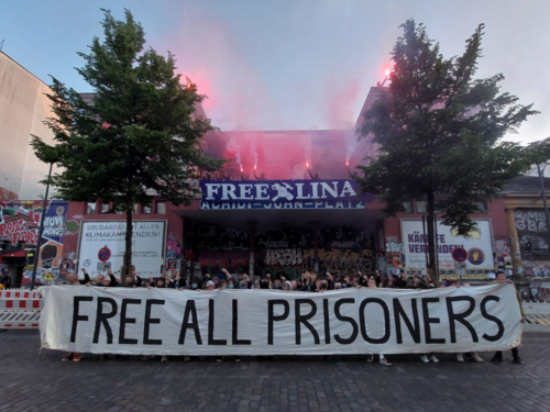 Eine Menge an Aktivist*innen findet sich zu einem Solifoto zusammen und hält Banner mit "Free Lina" & "Free All Prisioners"